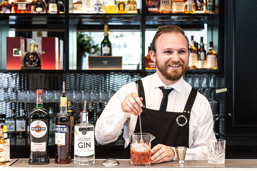 Bearded bartender mixing an old fashion in a bright lit modern bar