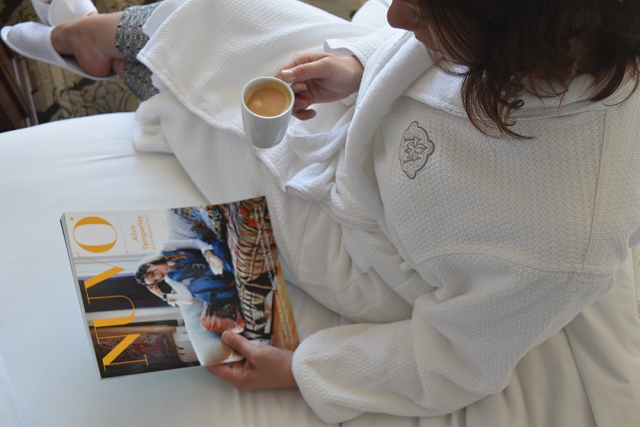 Women drinking Nespresso while reading NUVO magazine in bed, wearing Magnolia embroidered house coat.