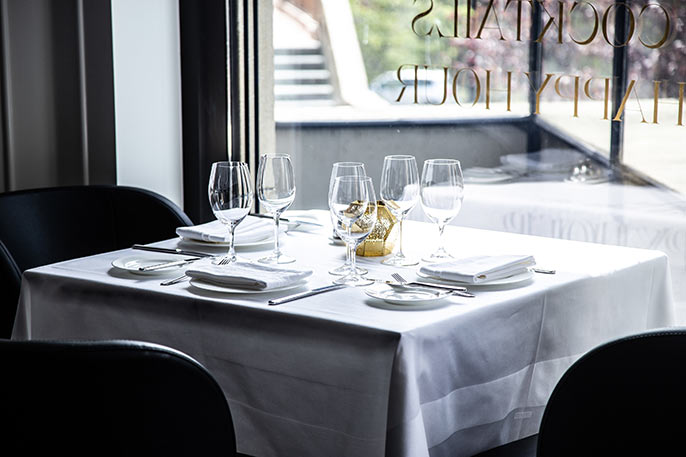 dining table with white tablecloth in front of window with the words cocktails and happy hour written on it.