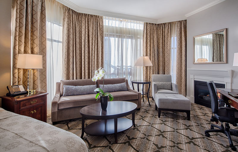 Large corner room with sitting area couch and chair with ottaman by fireplace near computer desk. White orchid on low coffee style table.