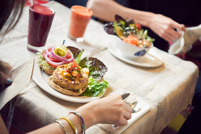 2 people at table eating veggie burger and veggie bowl with glasses of fresh jus