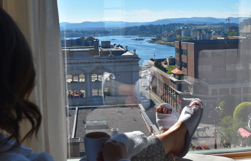 aha moment, women with slippers, feet, drinking coffee looking out grand window with view of water, buildings, and Victoria life.