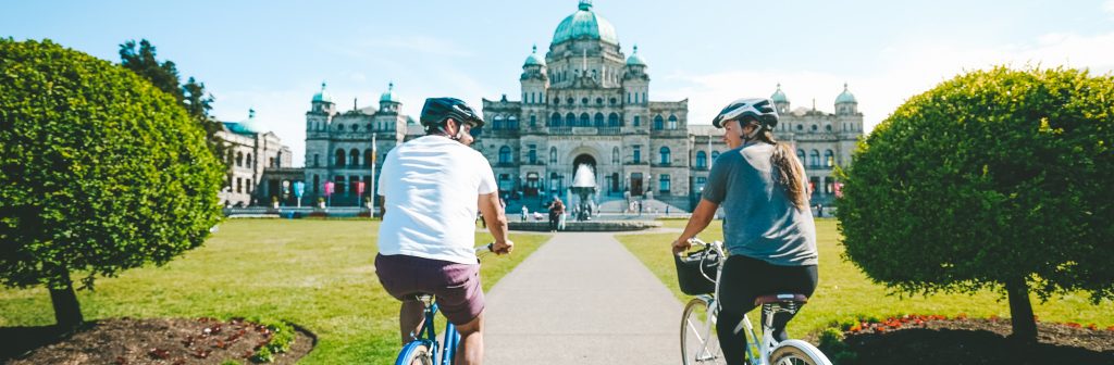 Women and man riding bikes towards the parliament buildings on sunny day